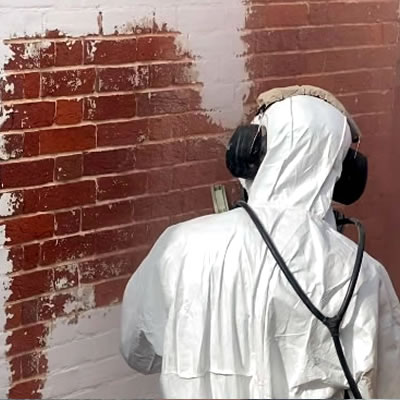 Person using a blasting nozzle carefully removing paint from a brick wall